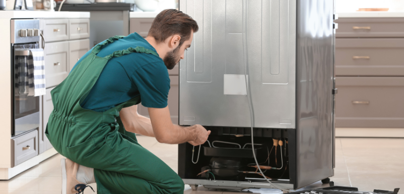 Técnico de refrigeração consertando geladeira.